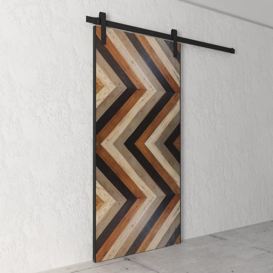 Urban Woodcraft Chevron Barn Door - Cali (3) The Chevron, Reclaimed Wood Barn Door (83" x 40") with a chevron pattern of varying shades of brown and black is mounted on a white textured wall.