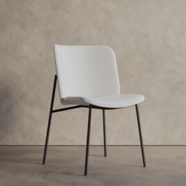 The Castello Dining Table - Natural stands on a plain floor against a neutral textured wall, showcasing its modern design and natural finish.