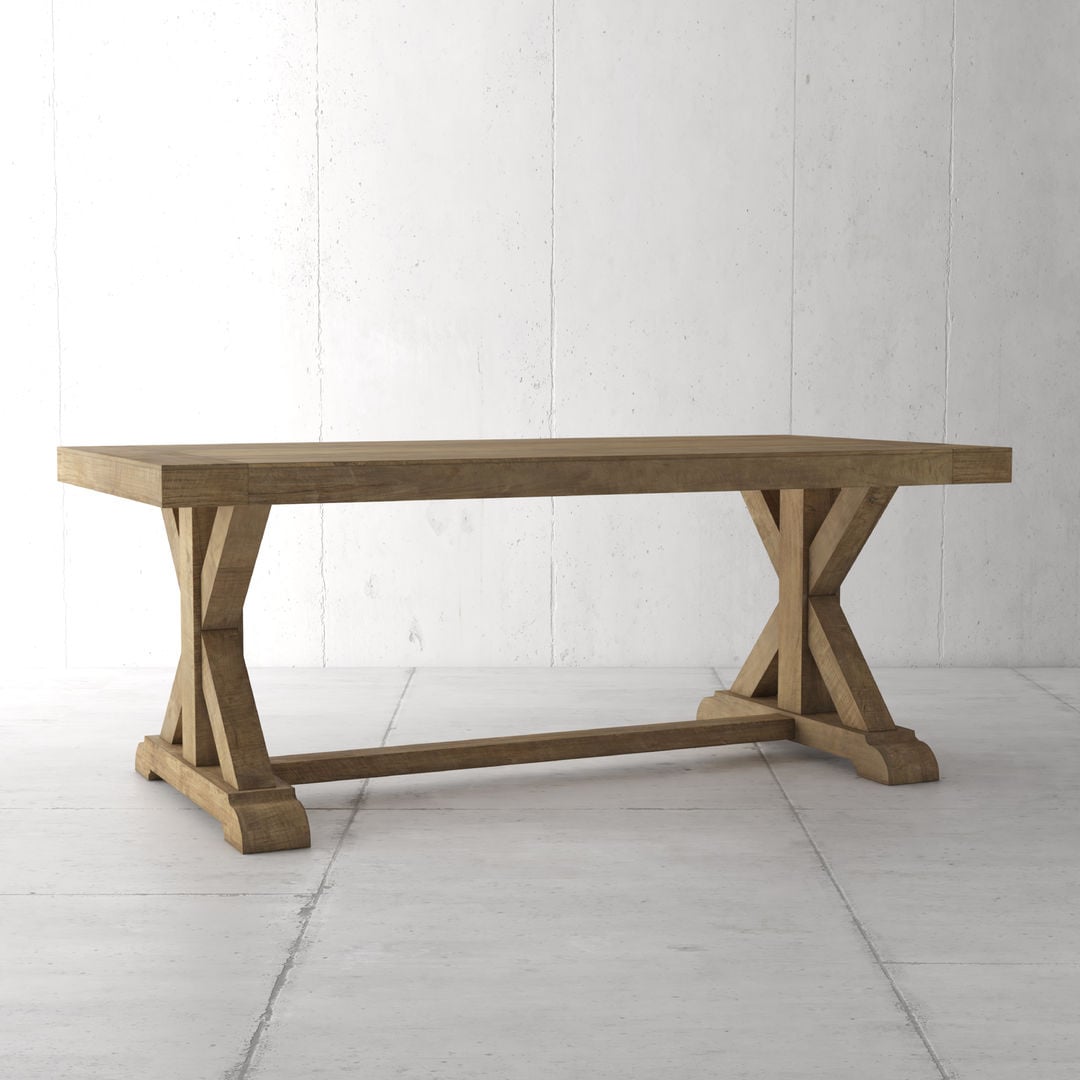 A wooden table with an X-brace design on the legs stands against a plain, light-colored wall and floor.