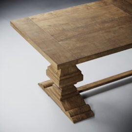 Close-up of the Castello Dining Table - Natural, featuring a thick rectangular wooden top and an ornate tiered pedestal base, set on a light grey surface.