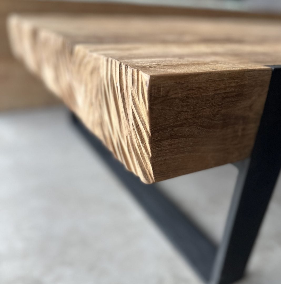 Close-up of the Hudson Coffee Table’s wooden edge with a carved texture, supported by a black metal leg on a light-colored floor.