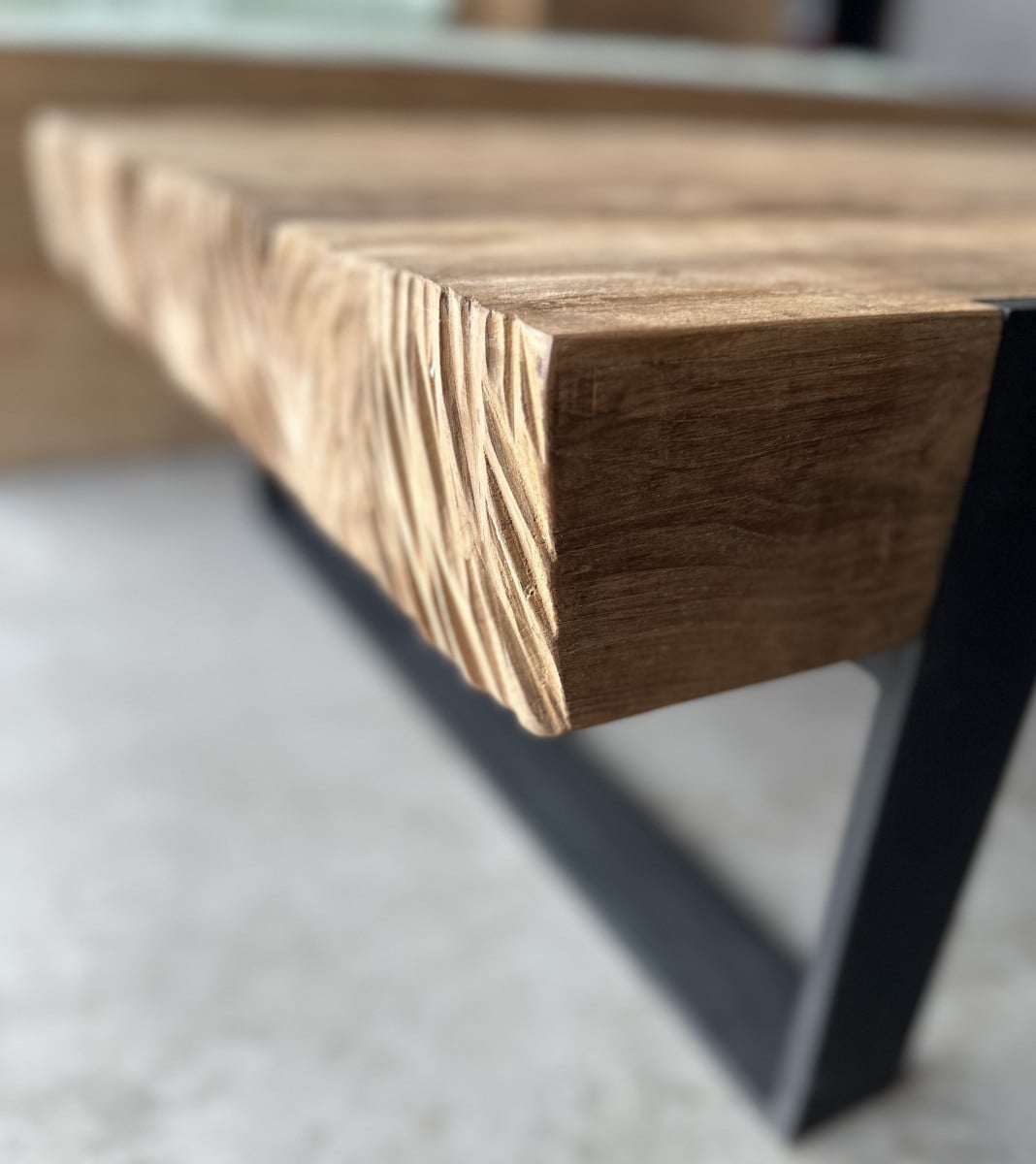 Image_20250806_174108_958 Close-up of the Hudson Coffee Tableโs wooden edge with a carved texture, supported by a black metal leg on a light-colored floor.