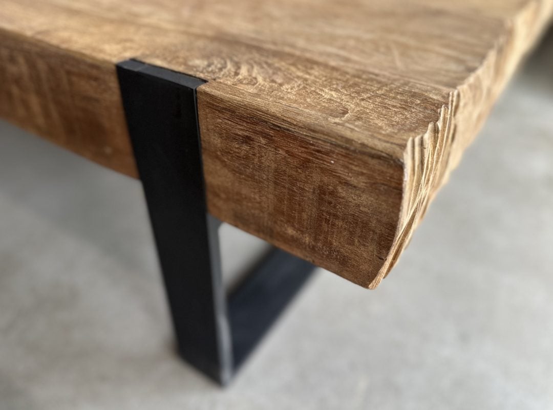 Image_20250806_174109_718 Close-up view of the Hudson Coffee Table, featuring a wooden top with a rough, unfinished edge and a black metal leg, set on a concrete floor.