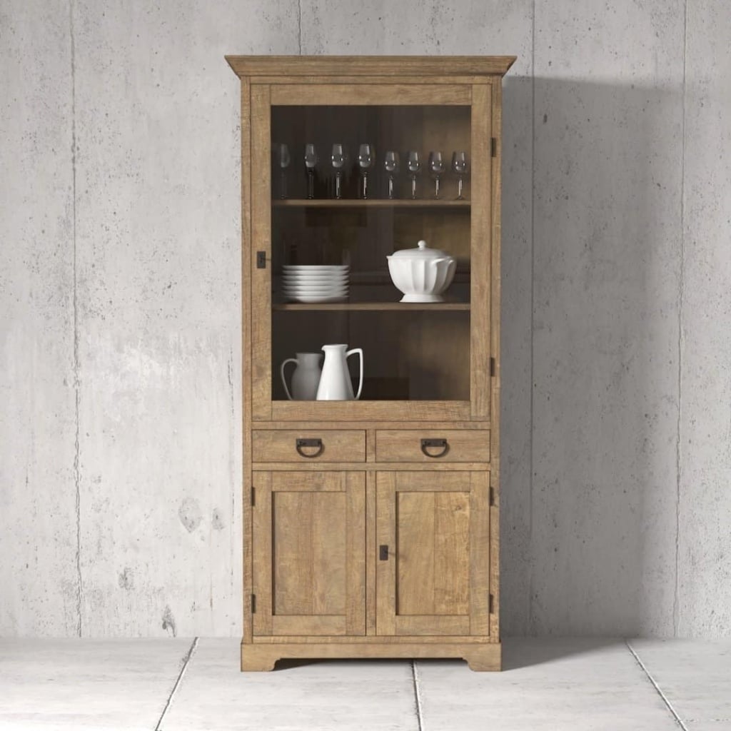 A wooden cabinet with a glass door on the upper section displaying glasses and plates, and a solid lower section with two drawers and two doors, placed against a concrete wall.