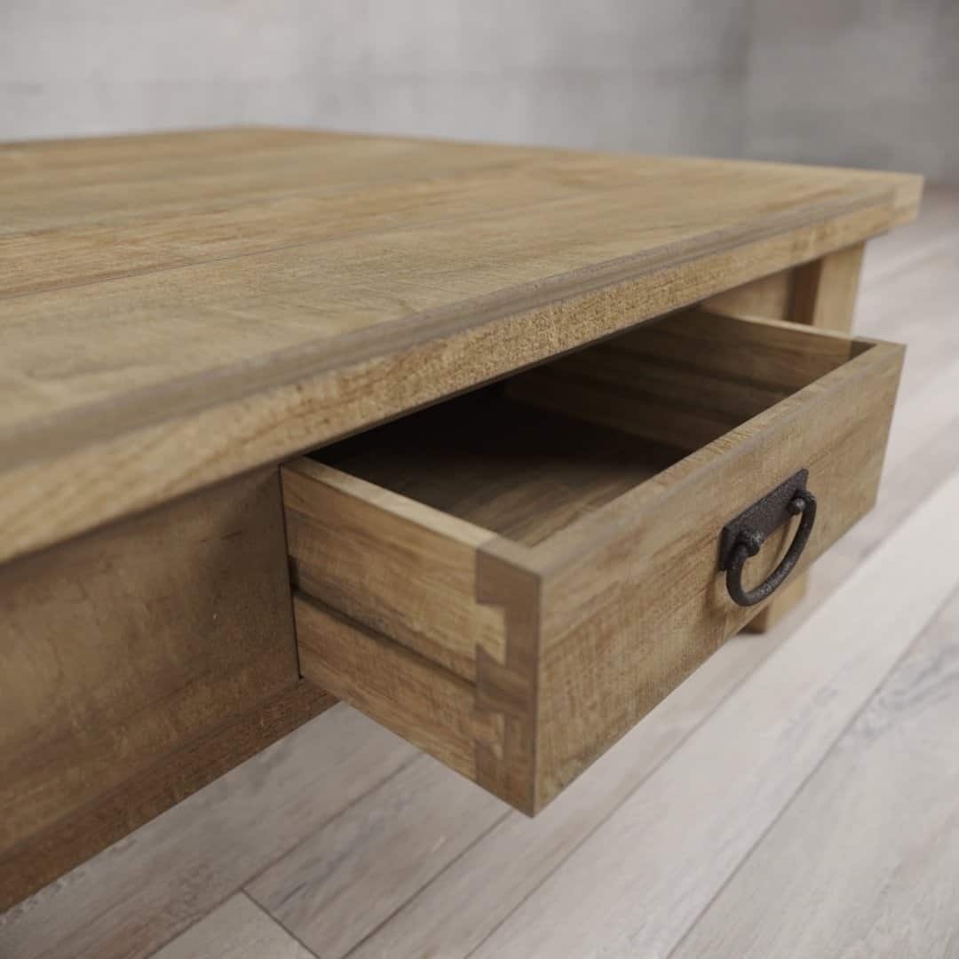 Urban Woodcraft 40 Riverbend Coffee Table - Natural (6) A close-up of the Riverbend Coffee Table with an open drawer. The table is crafted from light-colored wood and features a metal handle on the drawer. The floor is adorned with light-colored wooden planks.