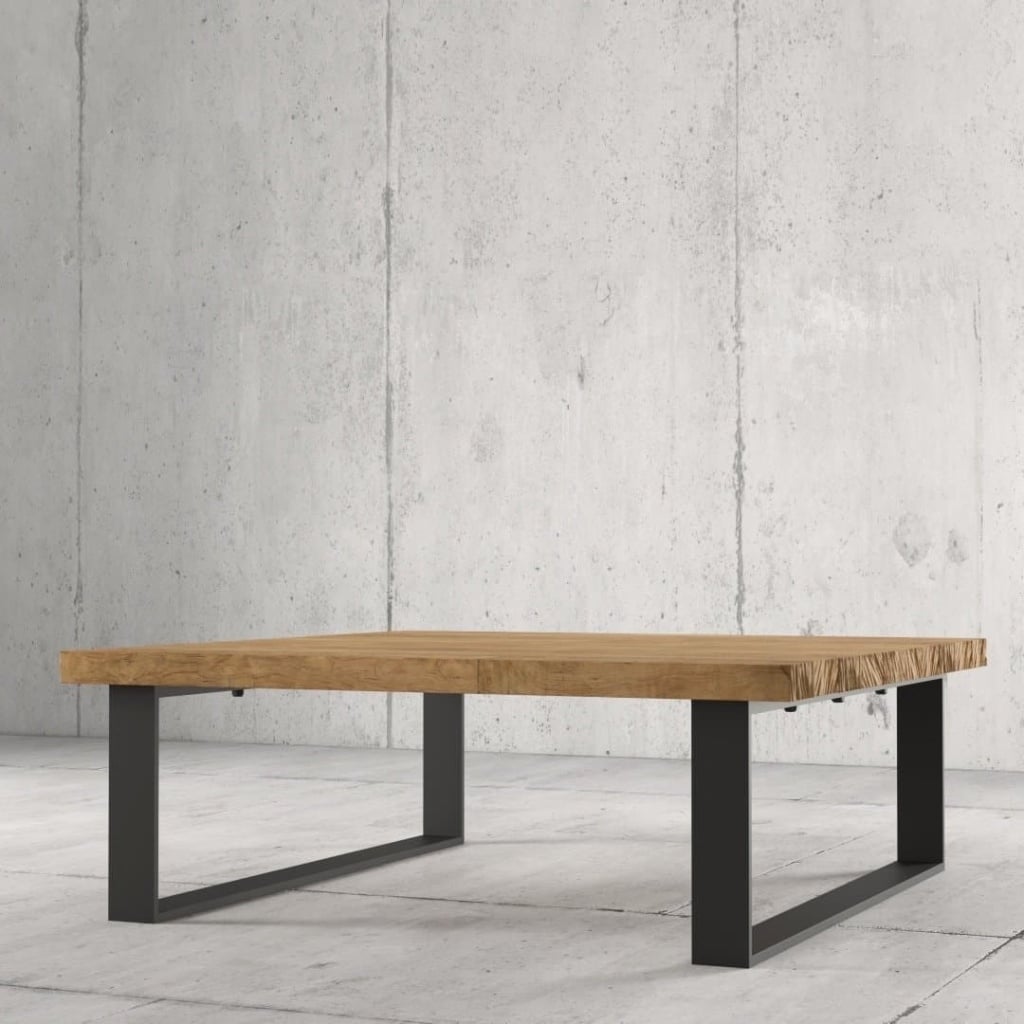 The Soma Coffee Table, featuring a thick rectangular wooden top and black metal legs, stands on a concrete floor against a concrete wall.