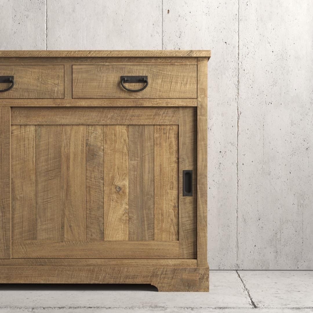 Urban Woodcraft 65 Riverbend Dining Buffet - Natural (4) The Riverbend Sliding Door Dining Buffet is a wooden cabinet with a light, natural finish, featuring two drawers with metal handles and a large cupboard door, set against a concrete wall.
