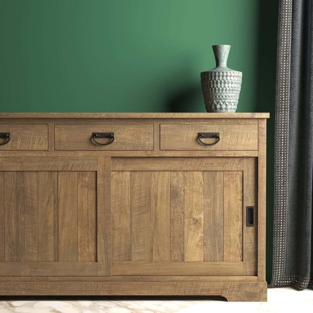 Urban Woodcraft 65 Riverbend Dining Buffet - Natural Livestyle Riverbend Sliding Door Dining Buffet featuring three drawers and two sliding doors, adorned with a textured ceramic vase, positioned against a green wall near a window with dark curtains.