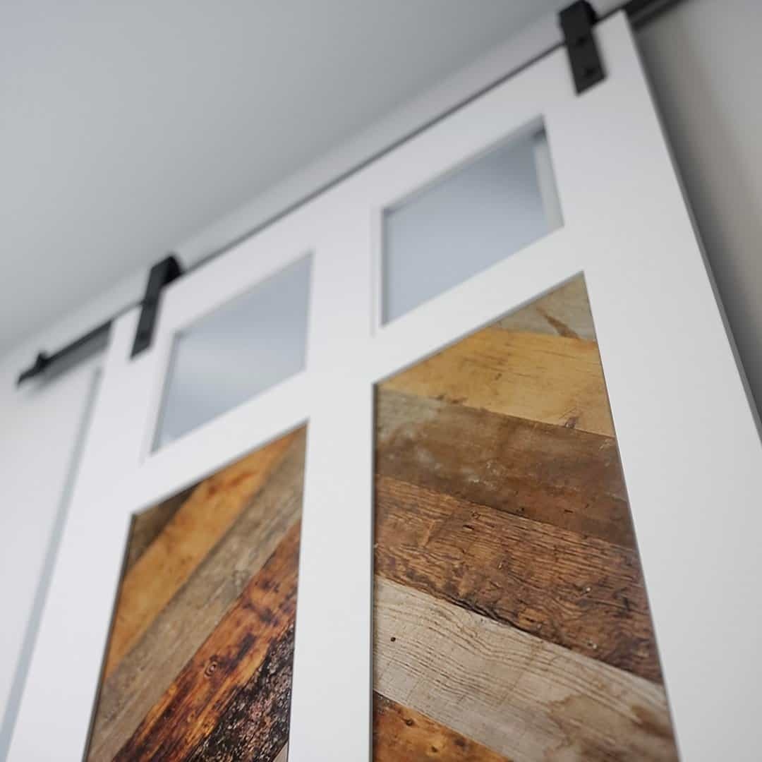 LAKEHOUSE RW (3) Close-up of the Lake House Barn Door, featuring frosted glass panels and wooden inserts, hung on a black metal rail.