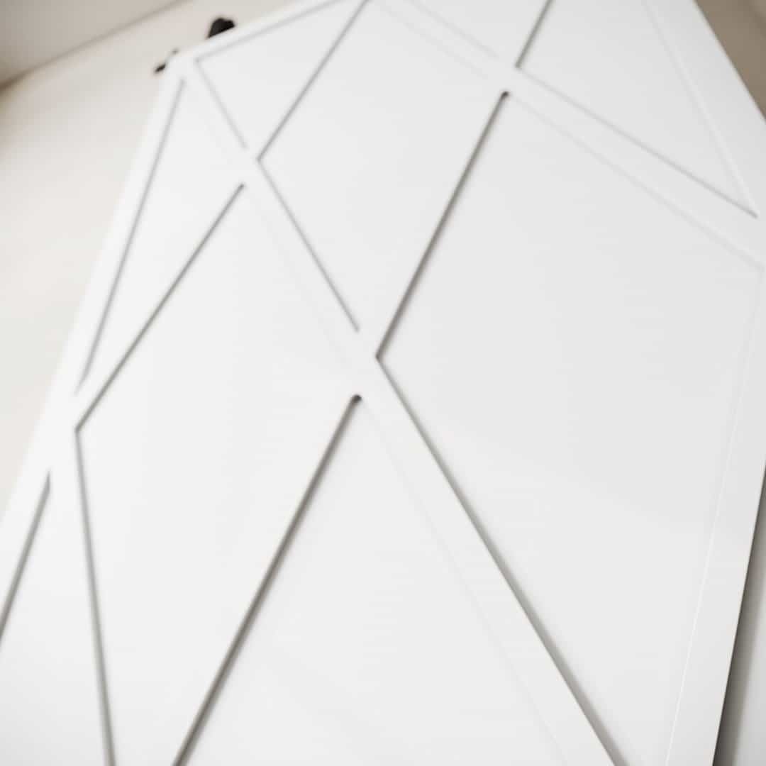 LYNX WHITE (3) A Lynx Barn Door, featuring geometric white surfaces with angular, intersecting lines, lies flat, partially propped against a white wall.
