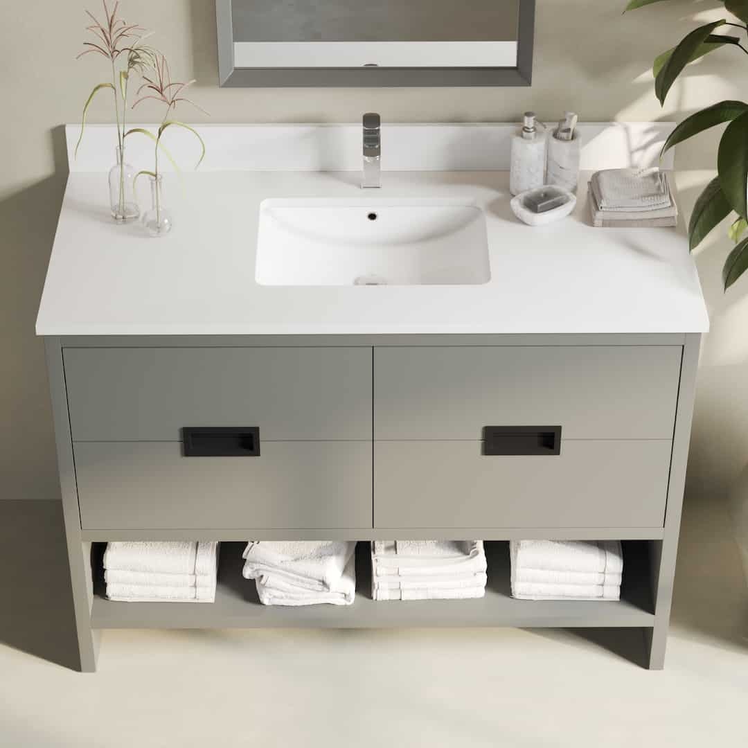 Urban Woodcraft Delamere 48in Single Bathroom Vanity Dark Grey 3 The Delamere 48" Single Sink Bathroom Vanity features a bathroom countertop with a rectangular sink, modern faucet, toiletries, and a plant. Its gray vanity includes drawers and has a shelf perfectly arranged with neatly folded white towels.
