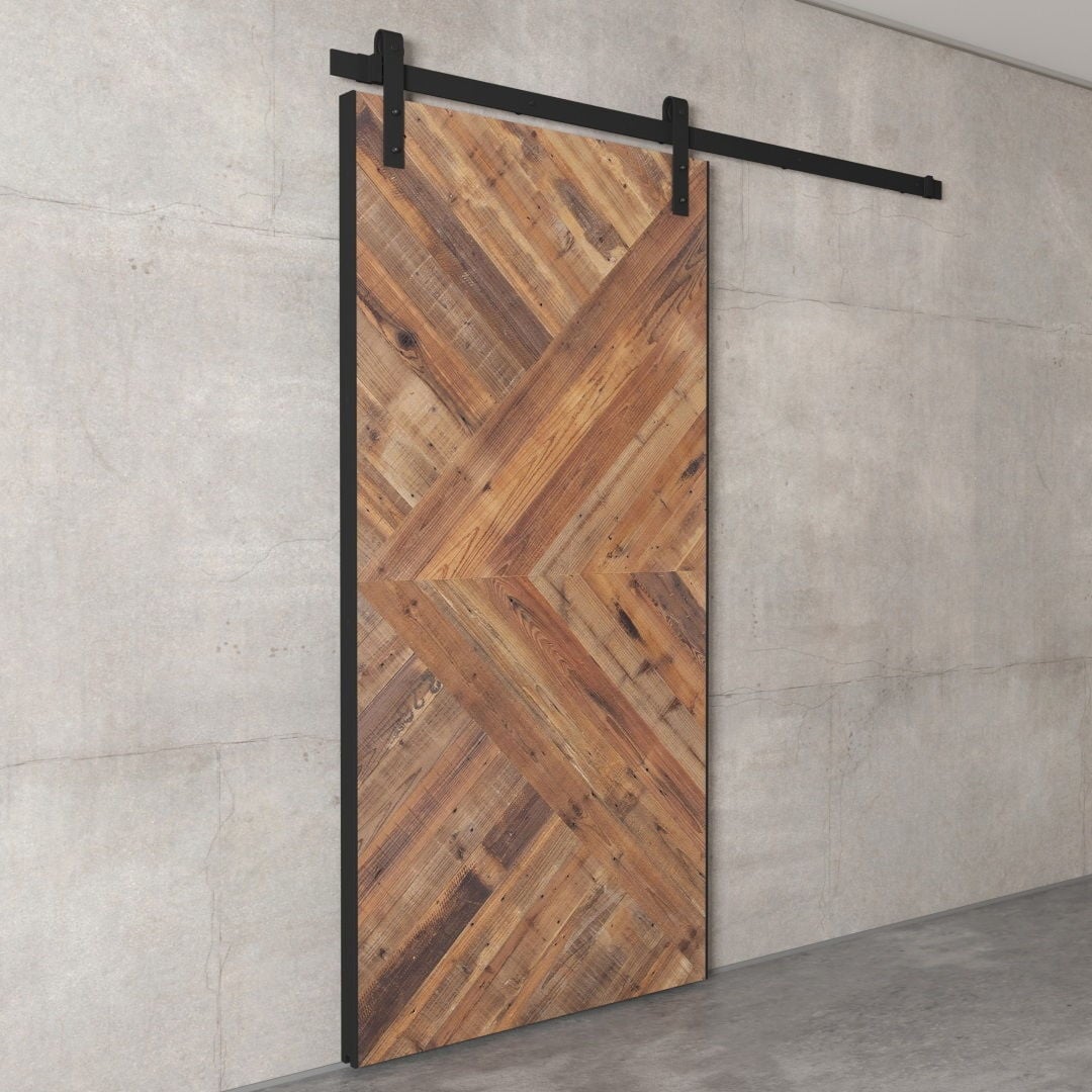 91x44 Custom Reclaimed Wood Arrow Barn Door (Image 3) A Custom 91" x 44" Reclaimed Wood Arrow Barn Door with a diagonal herringbone pattern is mounted on a black track, set against a grey concrete wall.