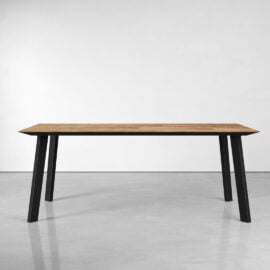 The Rectangle Kolt Dining Table, featuring a wooden surface and black metal legs, is positioned in an empty room with a white wall and light gray floor.