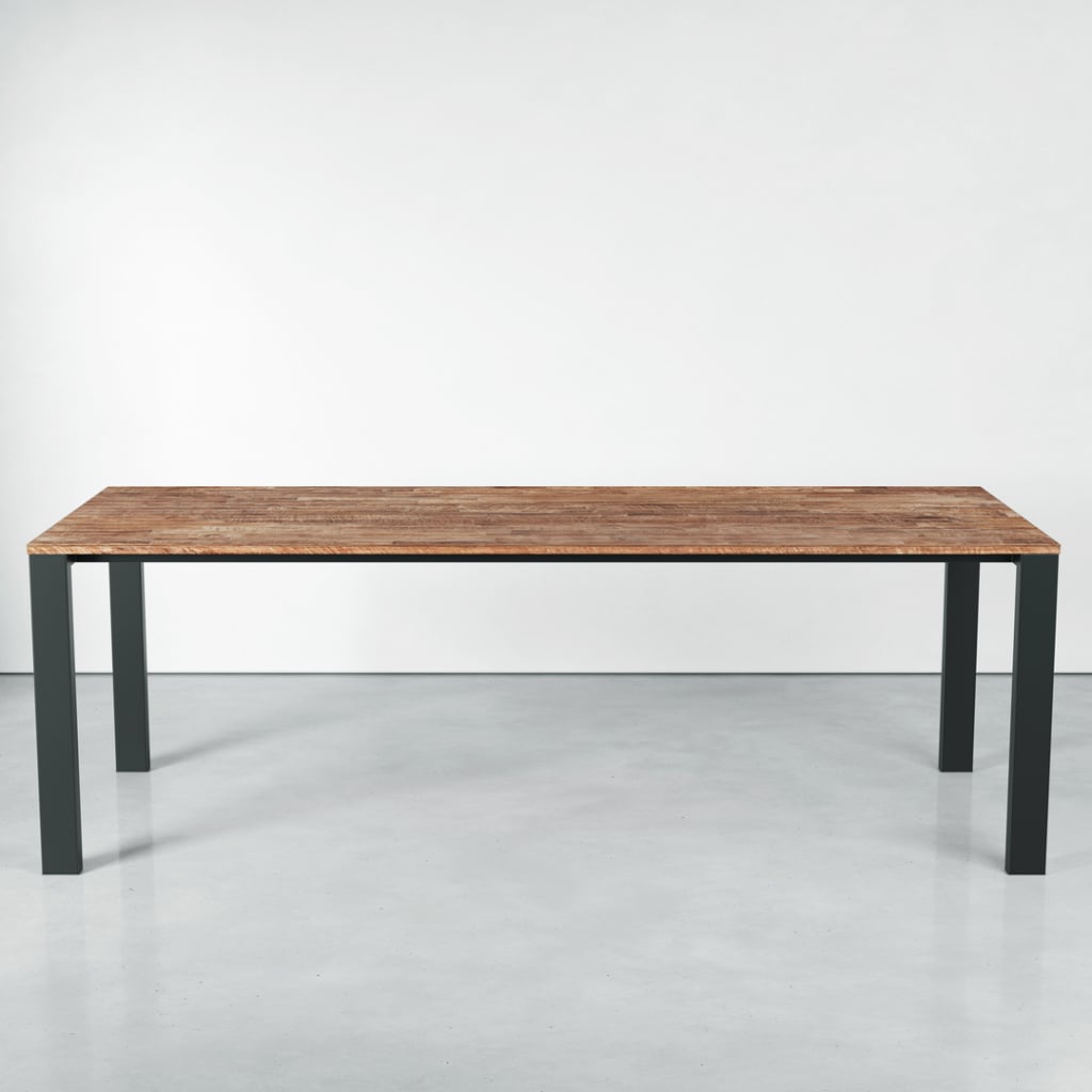 The Metal Dining Table, featuring a wooden rectangular top and black metal legs, stands on a smooth, light-colored floor against a plain white wall.