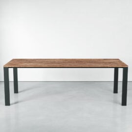 The Metal Dining Table, featuring a wooden rectangular top and black metal legs, stands on a smooth, light-colored floor against a plain white wall.