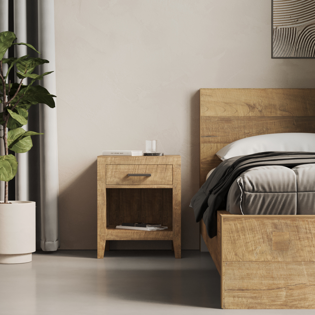 Riviera Nightstand - 3 The Riviera Nightstand, featuring a drawer and an open shelf, is positioned beside a bed with a wooden frame. A glass of water and a book rest on the nightstand, while a potted plant sits next to it.