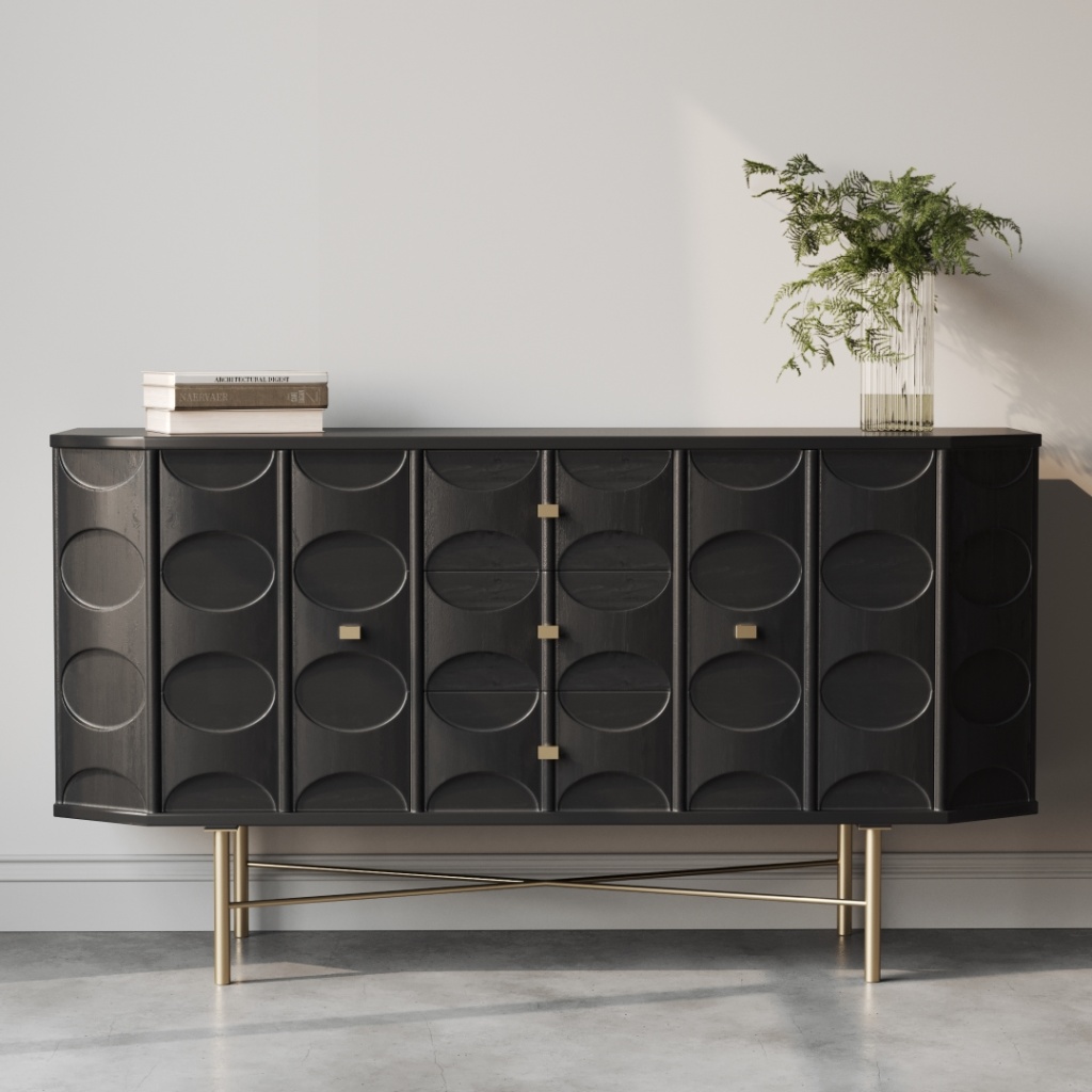 The Alba 60" Sideboard, featuring black oval patterns, four square handles, and gold legs, stands against a white wall. On top, there is a small stack of books and a glass vase with green foliage.