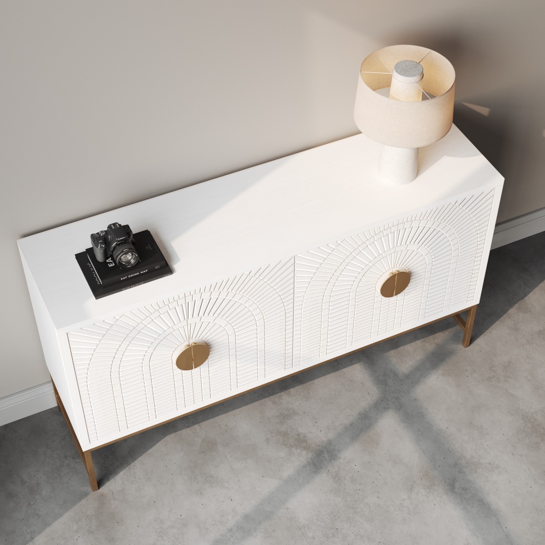 Coral 60 Side Cabinet -d The Coral 60" Sideboard, a white piece with gold accents, stands on a concrete floor near a wall. It features a camera and book on top, with a white lamp placed on the far right side.