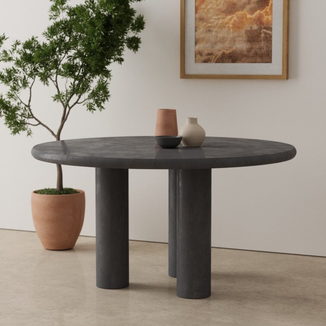 55 Aero Round Dining Table in black 2 The Aero Round Dining Table, featuring a dark gray finish and three cylindrical legs, is adorned with three vases. A potted plant and a framed art piece rest against the light wall in the background.