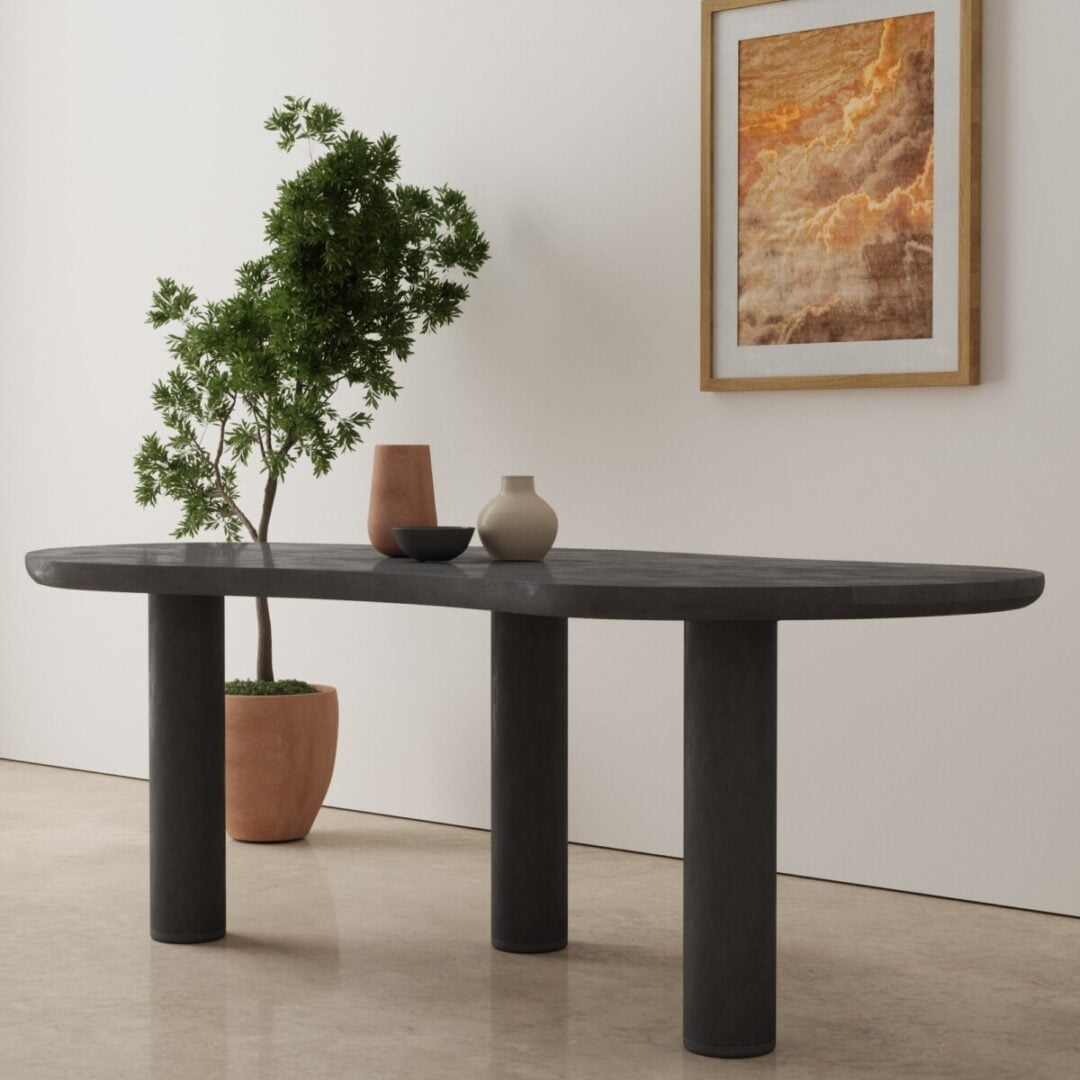 87 Aero Organic Dining Table in black 3 The Aero Organic Dining Table, an oval black table with three cylindrical legs, is styled with two vases on top, a potted plant beside it, and a framed landscape artwork on the white wall in a minimalist room.