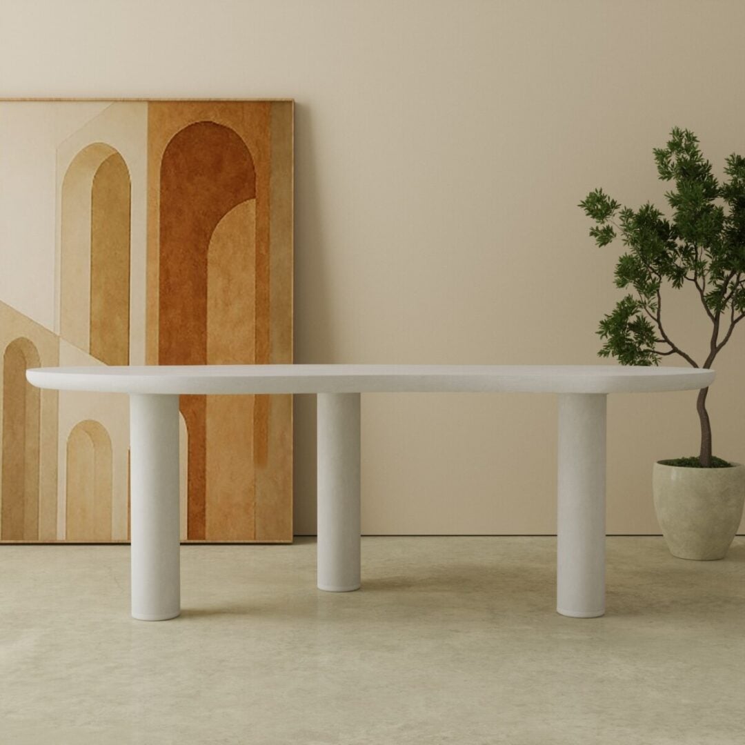 87 Aero Organic Dining Table in white 1 The Aero Organic Dining Table, a minimalist white oval design with cylindrical legs, stands on a beige floor beside a potted plant and an abstract arches painting.