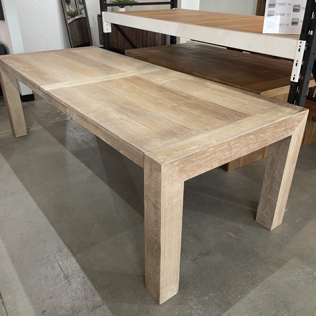 The Villa 98" Dining Table (Bleached White) is displayed on a concrete floor, featuring clean, simple lines and sturdy legs with a light, wooden finish.