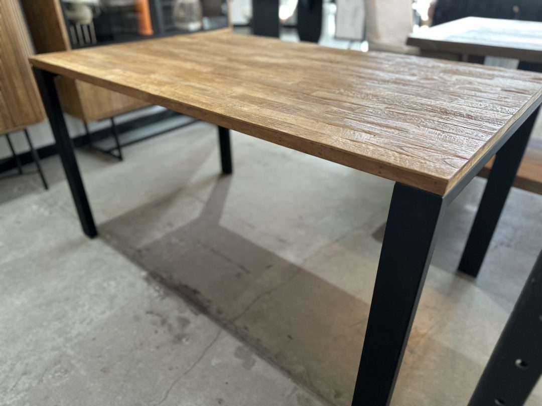 Image_20250806_174109_065 (1) The Metal Dining Table (Natural) features a rectangular wooden top with a textured finish and black metal legs, placed on a concrete floor in a modern indoor space.
