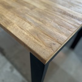 A close-up of the Metal Dining Table (Natural) shows its light wood finish and black metal legs set on a concrete floor.