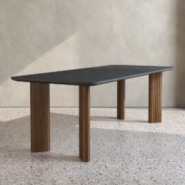 The Osaka 4 Pillar Dining Table features a dark rectangular tabletop and four vertically grooved wooden legs, set on a terrazzo floor against a light-colored wall.