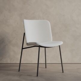The Kora 20" Dining Chair features a curved white seat and backrest with slim black metal legs, shown against a beige textured wall.