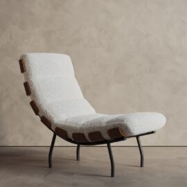 The Oslo 24" Lounge Chair features a white textured cushion, wooden side accents, and black metal legs, displayed against a beige textured wall.
