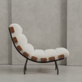 The Oslo 24" Lounge Chair features a curved black frame, white tufted upholstery, and exposed wooden side accents, set against a gray textured wall.