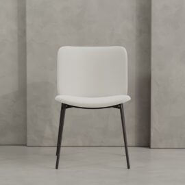 The Kora 20" Dining Chair features modern white upholstery and black metal legs, shown against a light gray textured wall.