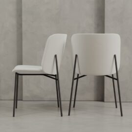 Two Kora 20" Dining Chairs in modern white with black metal legs are positioned in front of a gray textured wall; one is shown from the side, the other from the back.