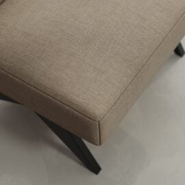 A close-up of the Laurel 27" Lounge Chair shows its beige upholstered cushion and black angled legs, set on a light-colored floor.