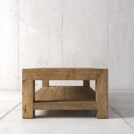 A rectangular wooden coffee table with a lower shelf, placed on a light-colored concrete floor against a textured white wall.
