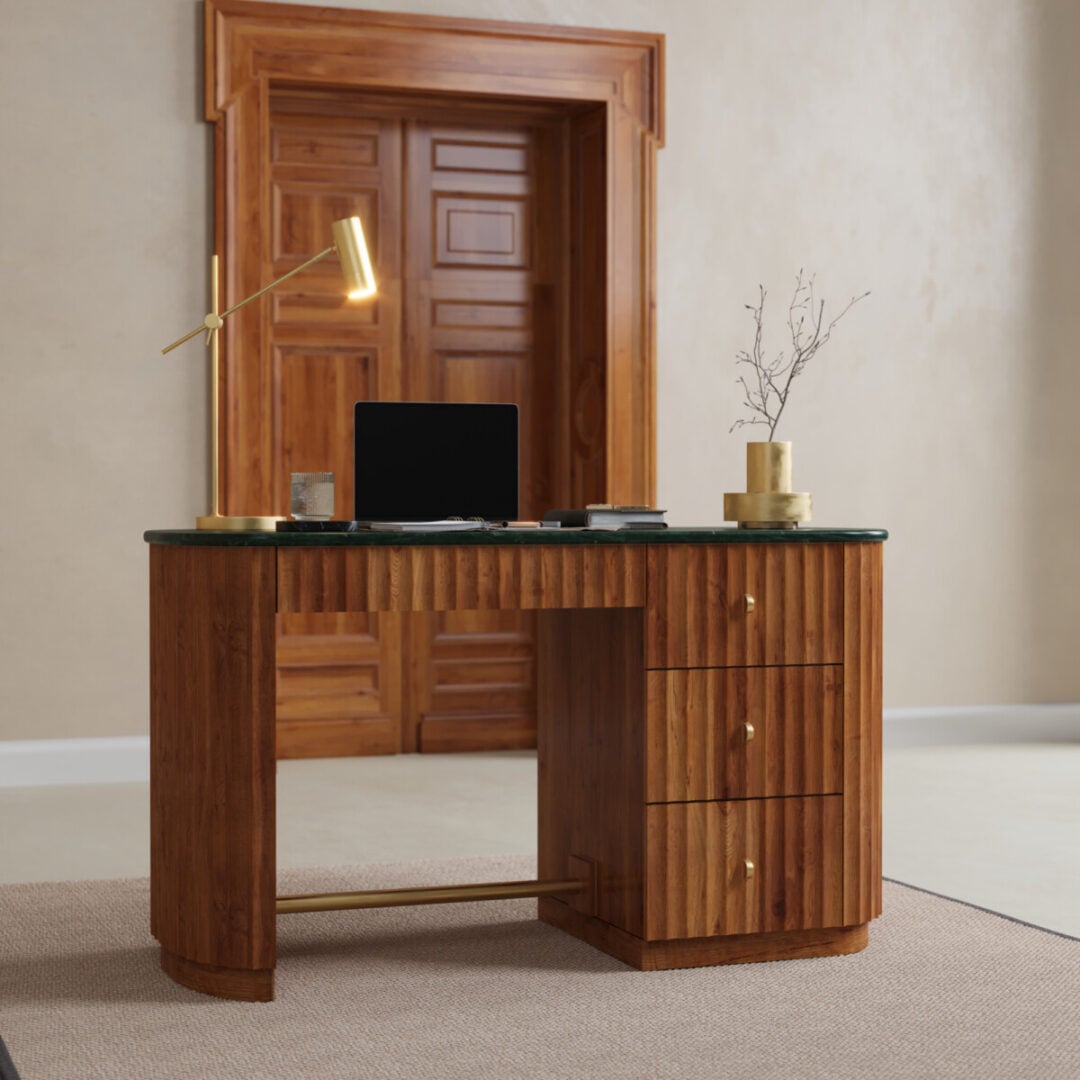 Elma 53-in. Desk-02 The Elma Desk, featuring drawers, holds a laptop, desk lamp, notebook, and vase on a rug in front of a wooden door in a minimalist room.