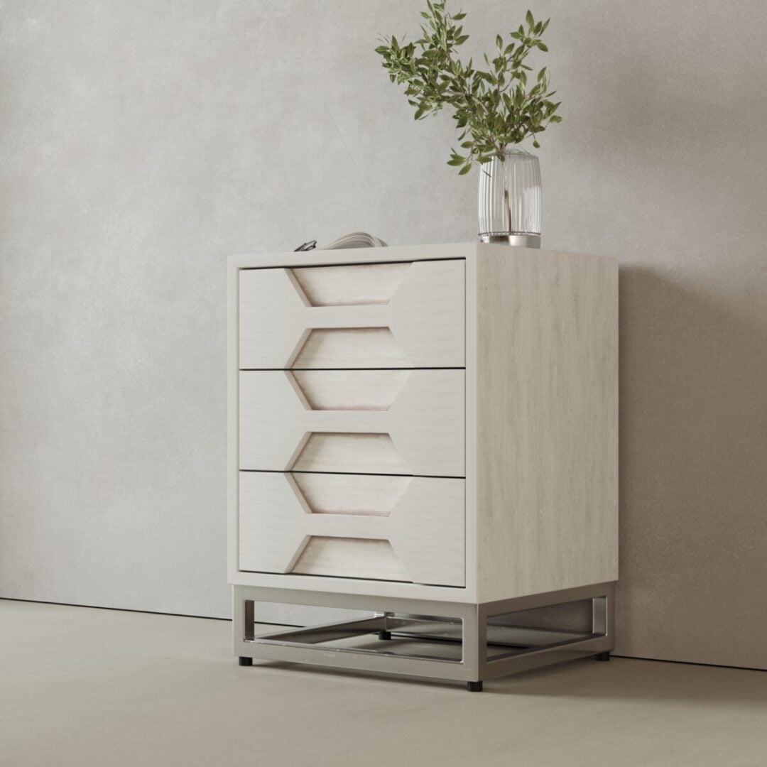 The Vexa Nightstand features a modern, light wood design with three geometric drawers, a metal base, and is topped with a clear vase of green foliage against a plain light-colored wall.