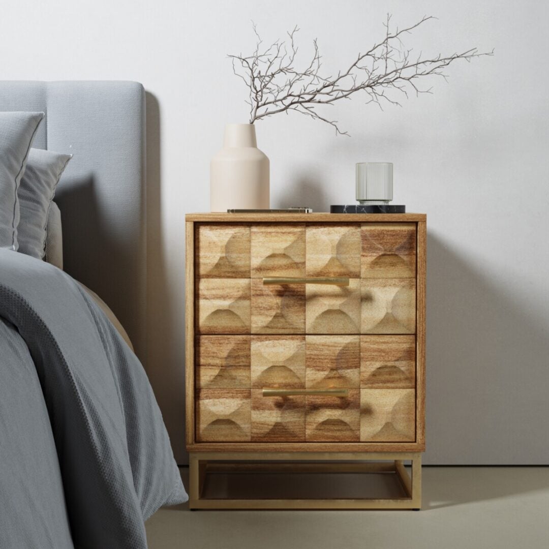 The Wadi Nightstand features geometric-patterned drawers and is styled with a beige vase of bare branches, a glass candle, and a black book, positioned next to a gray bed.