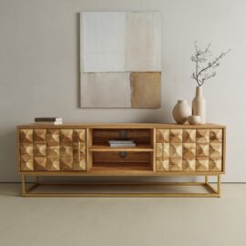 The Wadi TV Stand features geometric patterned doors and a gold metal base, topped with books and neutral vases, all beneath a minimal abstract painting.