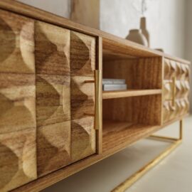 Close-up of the Wadi TV Stand featuring textured geometric wooden doors, gold handles, open shelving, and gold metal legs; decorative vases and books are displayed on and inside the unit.
