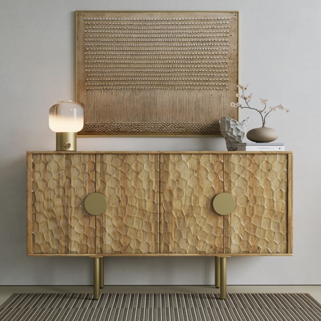 The Luna Sideboard, featuring textured wooden doors, stands against a light wall with a glass lamp, ceramic vase, and decorative object on top. A woven artwork hangs above it.