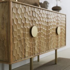 The Luna Sideboard, featuring a honeycomb-patterned front, round gold handles, and gold legs, is displayed on a textured rug.