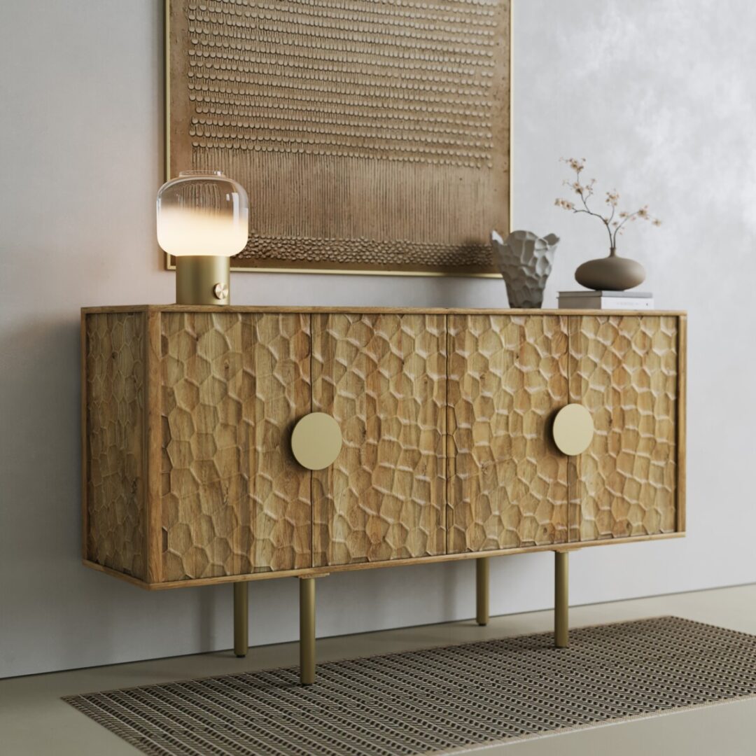 Luna Sideboard-04 The Luna Sideboard, featuring a textured geometric design, large round handles, and gold legs, is styled with a lamp, vase, and decor. It stands against a neutral wall beneath framed artwork.