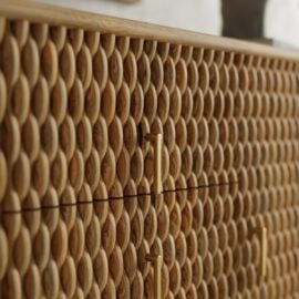 Close-up of a wooden cabinet with a textured, oval-patterned surface and vertical gold handles.