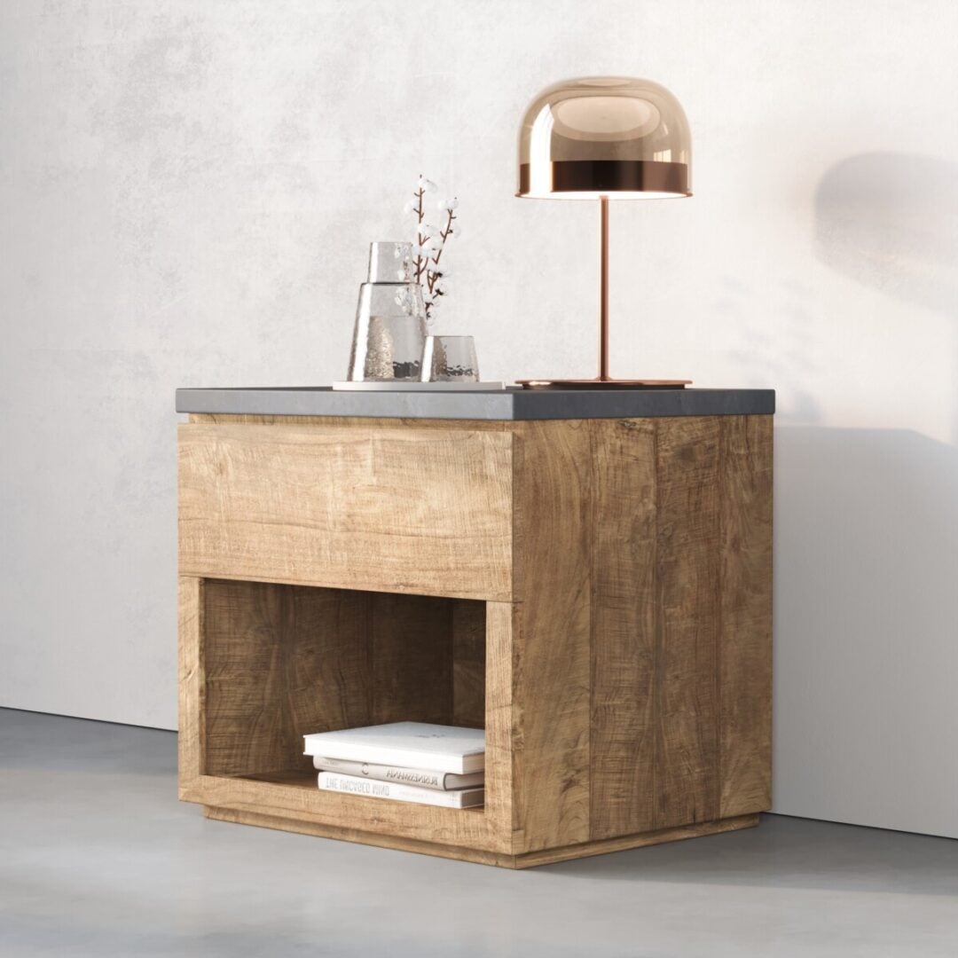 The Nox Nightstand, featuring an open shelf with two books, is topped with a clear vase of branches, a glass carafe, and a metallic lamp, all set against a white wall.