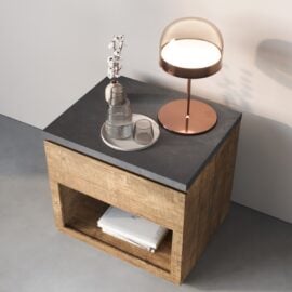 The Nox Nightstand with a black top holds a round lamp, a tray with a glass jug, two glasses, and a small vase; a book rests on its lower shelf.
