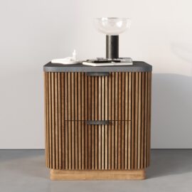 The Osaka Nightstand, featuring vertical slats, black handles, and a dark top, holds a glass bowl, books, and small items while standing against a plain light wall.