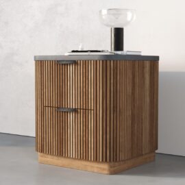 The Osaka Nightstand is a small wooden cabinet with vertical slats, a dark countertop, and is styled with a glass bowl and a black cylindrical object on top.